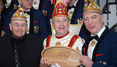 Bischof Dr. Felix Genn, Prinz Jens I. und Generalprinzmarschall Paul Middendorf (von links) halten eine hälzerne Tafel mit der Aufschrift "Pax Optima Rerum" in den Händen.