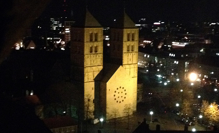 Der St.-Paulus-Dom wird in der Dunkelheit von außen mit Scheinwerfern angestrahlt.
